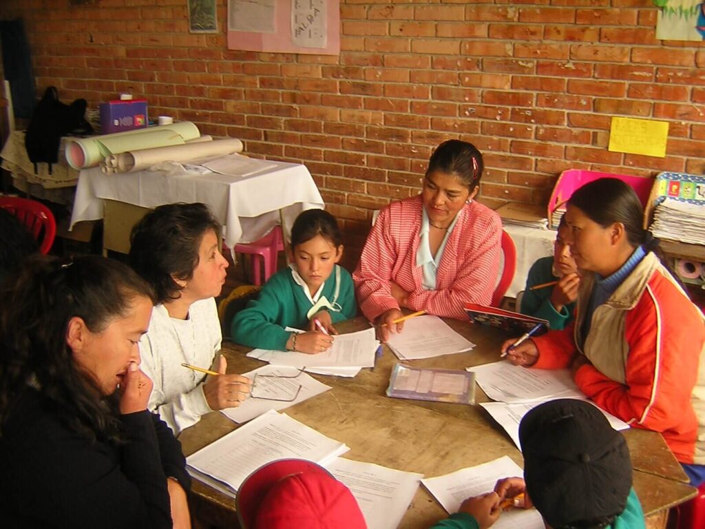 Un grupo de maestras y niños trabajan en equipo en una mesa.