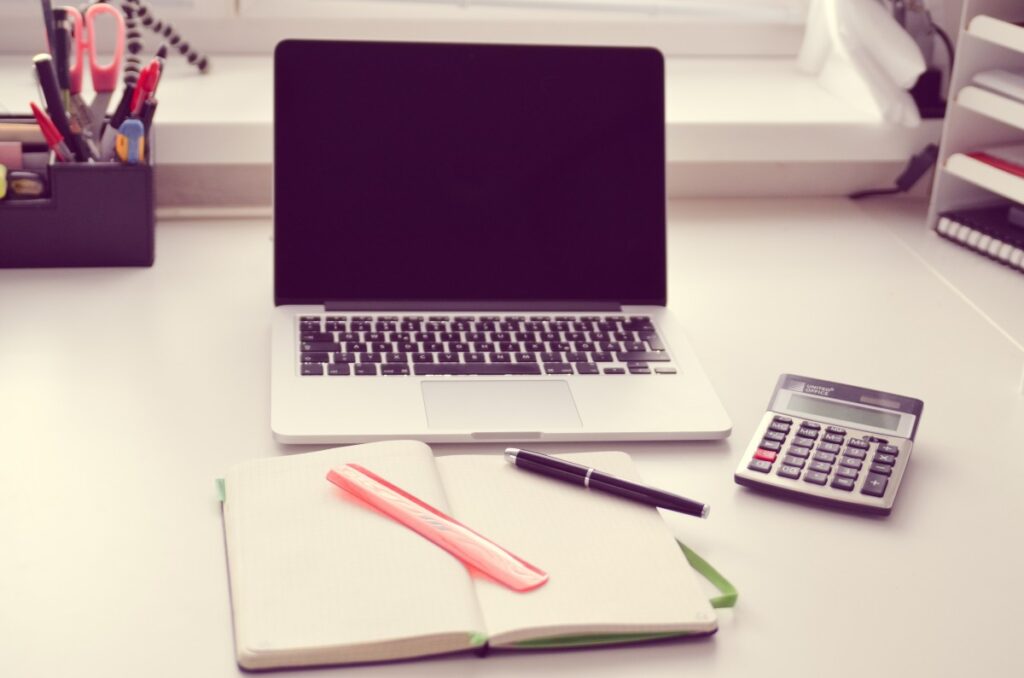 una laptop, una libreta, una pluma, una regla y una calculadora sobre un escritorio