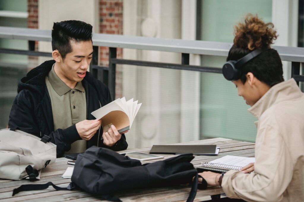 dos estudiantes trabajando con sus cuadernos y libros en una mesa al exterior
