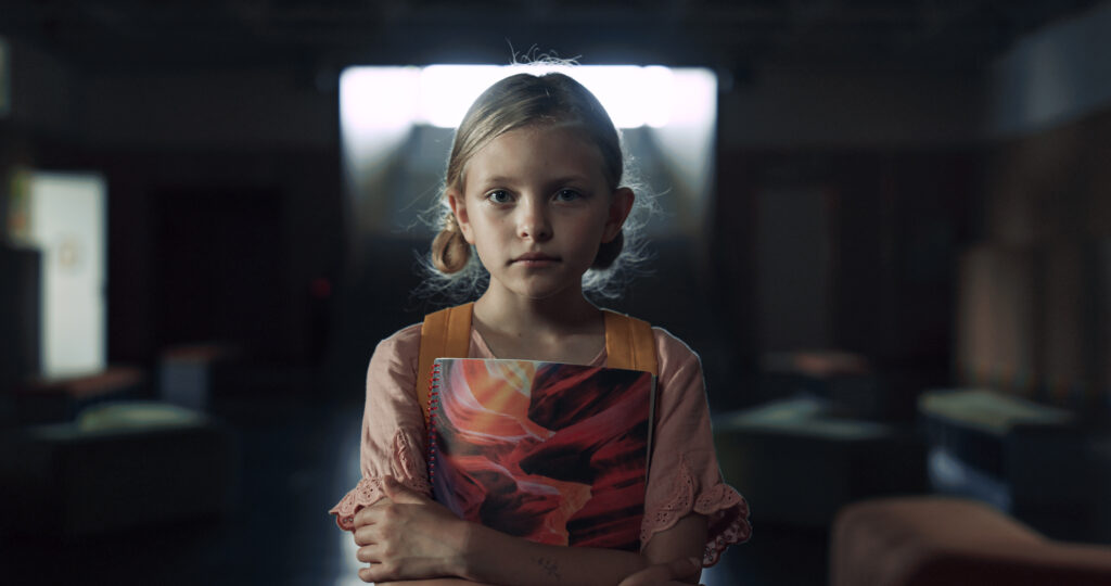 niña sosteniendo una libreta en una escuela destruida
