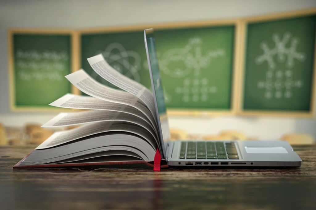 half book and laptop are merged together and sitting on a desk in a classroom.