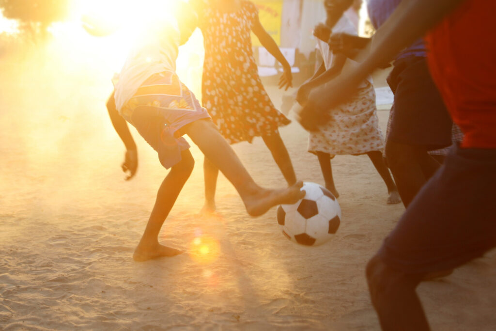 Niños de distintas nacionalidades jugando futbol en un campo de tierra
