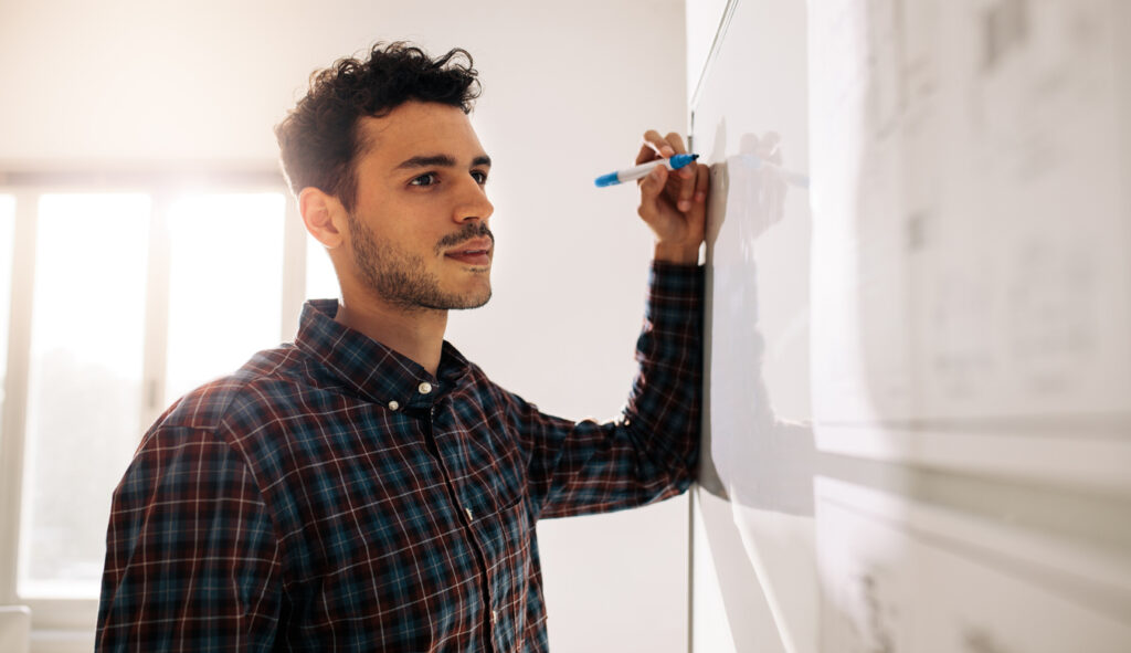 Businessman standing near a whiteboard holding a marker pen in office. Entrepreneur discussing business ideas and plans on a board.